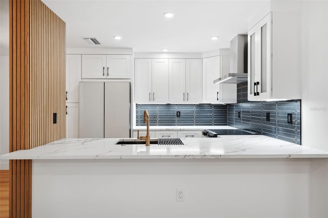 kitchen with fridge, sink, kitchen peninsula, and wall chimney exhaust hood