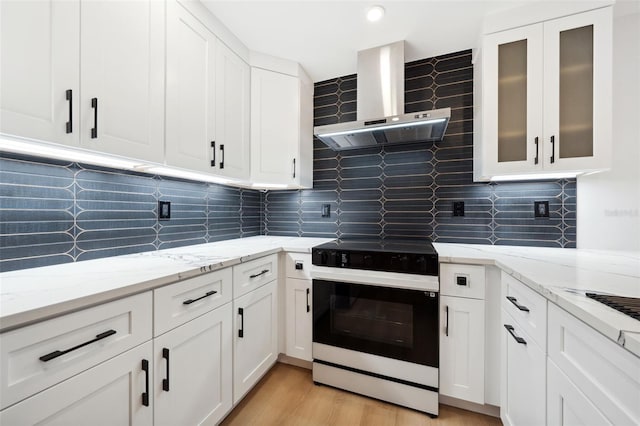 kitchen featuring white cabinetry, electric range oven, light stone counters, light hardwood / wood-style floors, and wall chimney exhaust hood