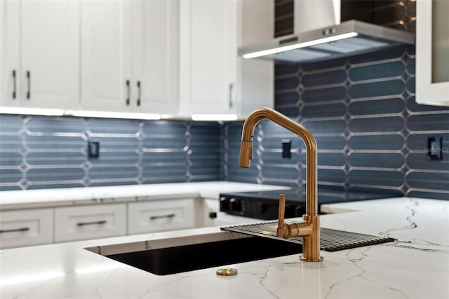 interior space with white cabinetry, rustic walls, backsplash, light stone counters, and wall chimney exhaust hood