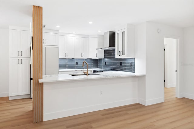 kitchen with sink, white cabinets, kitchen peninsula, wall chimney range hood, and light wood-type flooring