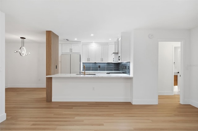 kitchen with white cabinetry, stainless steel fridge, kitchen peninsula, and sink