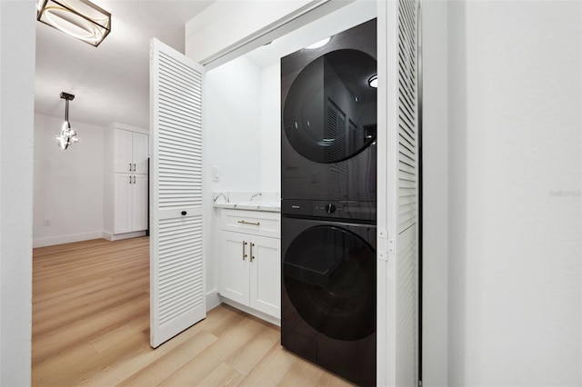 laundry room with stacked washer / drying machine and light wood-type flooring