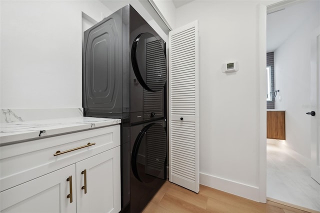 clothes washing area with cabinets, stacked washer and dryer, and light hardwood / wood-style flooring