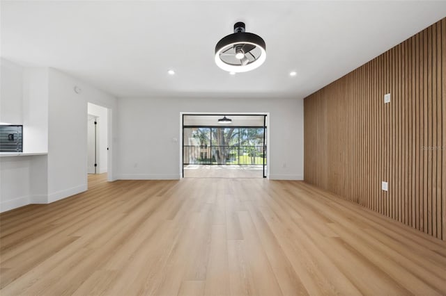 unfurnished living room with light wood-type flooring and wood walls