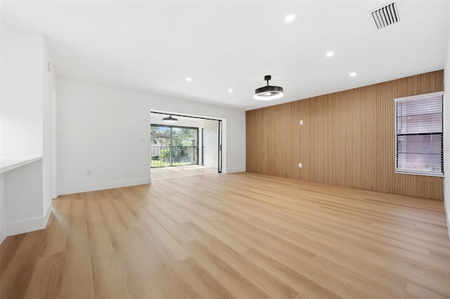 unfurnished living room featuring wooden walls and light hardwood / wood-style flooring