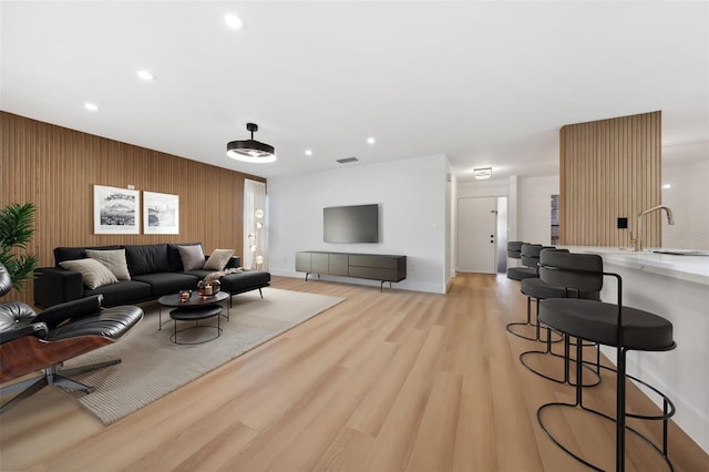 living room with sink, wooden walls, and light wood-type flooring