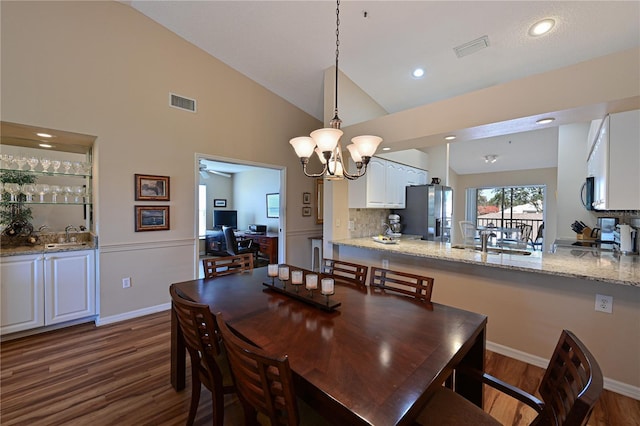 dining space with dark hardwood / wood-style flooring, sink, high vaulted ceiling, and an inviting chandelier