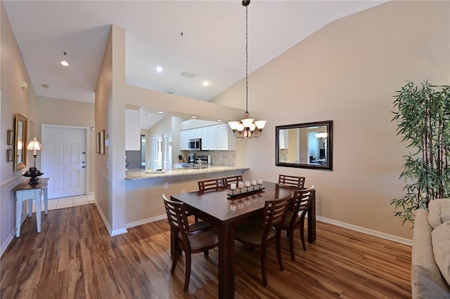 dining space featuring dark hardwood / wood-style flooring, high vaulted ceiling, and an inviting chandelier