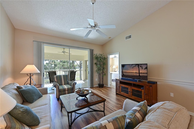 living room featuring ceiling fan, wood-type flooring, vaulted ceiling, and a textured ceiling