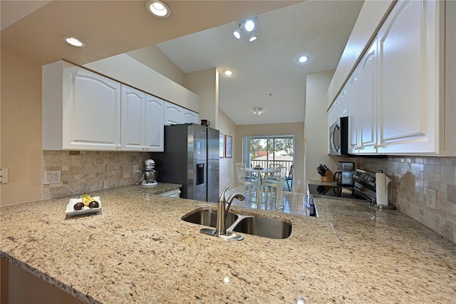 kitchen with sink, light stone counters, kitchen peninsula, stainless steel appliances, and white cabinets