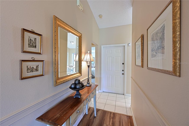 doorway to outside featuring vaulted ceiling, light wood-type flooring, and a textured ceiling