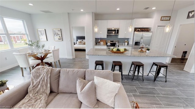 kitchen featuring pendant lighting, appliances with stainless steel finishes, a kitchen island with sink, a kitchen breakfast bar, and white cabinets