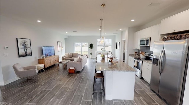 kitchen with a kitchen breakfast bar, an island with sink, pendant lighting, stainless steel appliances, and white cabinets