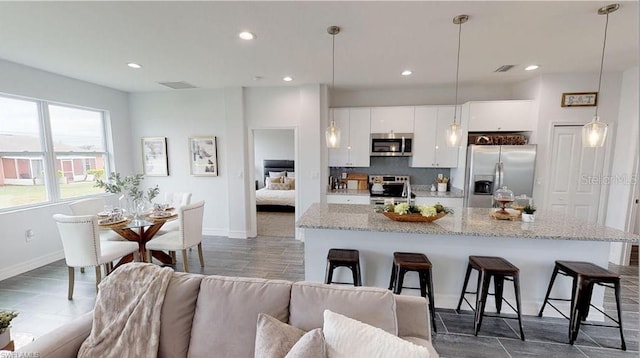 kitchen with pendant lighting, a breakfast bar, appliances with stainless steel finishes, white cabinets, and decorative backsplash