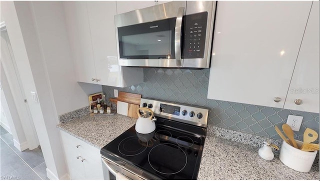 kitchen with backsplash, light stone countertops, white cabinets, and appliances with stainless steel finishes