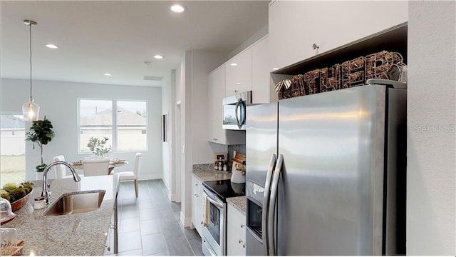 kitchen featuring sink, stainless steel appliances, light stone counters, white cabinets, and decorative light fixtures