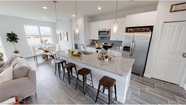 kitchen with appliances with stainless steel finishes, a breakfast bar, white cabinetry, an island with sink, and hanging light fixtures