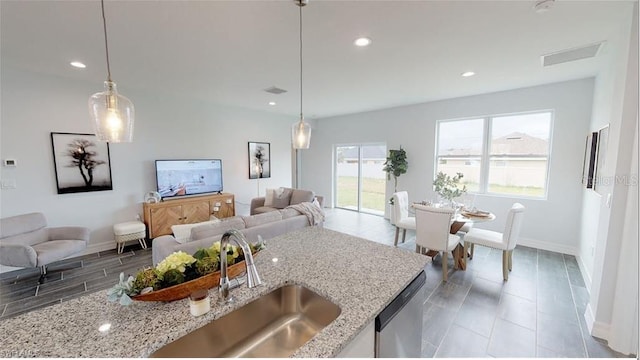 kitchen featuring light stone counters, stainless steel dishwasher, sink, and hanging light fixtures