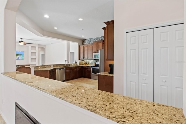 kitchen with sink, appliances with stainless steel finishes, kitchen peninsula, ceiling fan, and light stone countertops