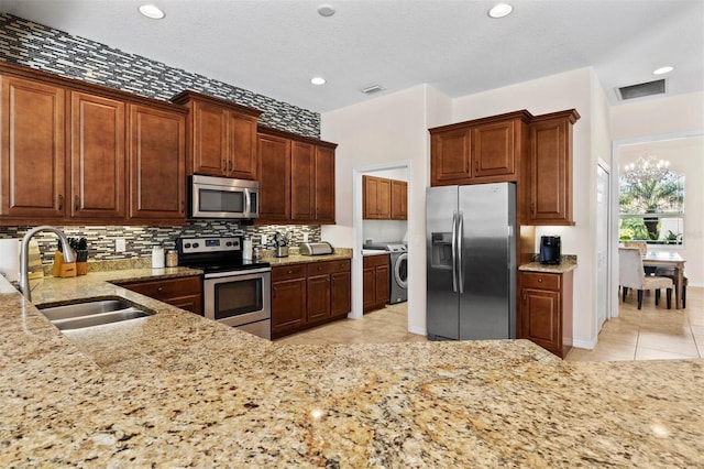 kitchen featuring sink, light tile patterned floors, appliances with stainless steel finishes, tasteful backsplash, and washer / clothes dryer