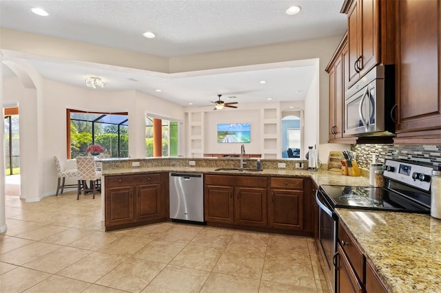 kitchen with sink, stainless steel appliances, light stone counters, decorative backsplash, and kitchen peninsula