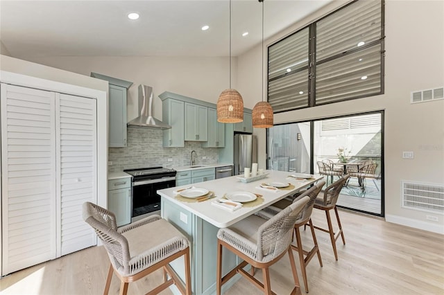 kitchen with a breakfast bar, sink, hanging light fixtures, stainless steel appliances, and wall chimney range hood