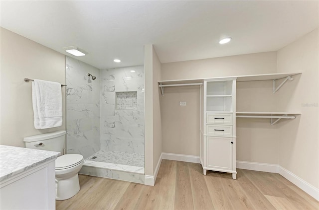 bathroom featuring vanity, tiled shower, hardwood / wood-style floors, and toilet