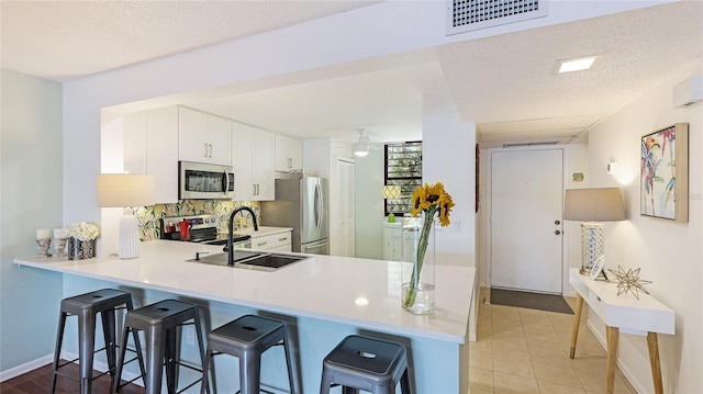 kitchen with sink, a breakfast bar, appliances with stainless steel finishes, white cabinets, and kitchen peninsula