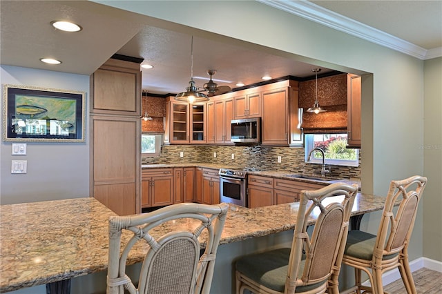 kitchen with a sink, appliances with stainless steel finishes, a kitchen bar, glass insert cabinets, and pendant lighting