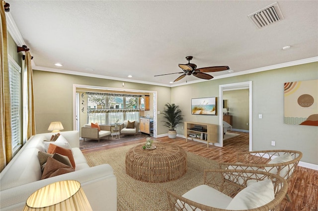 living room featuring hardwood / wood-style flooring, ornamental molding, a textured ceiling, and ceiling fan