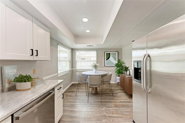 kitchen with white cabinetry, light stone counters, light wood-type flooring, appliances with stainless steel finishes, and a tray ceiling