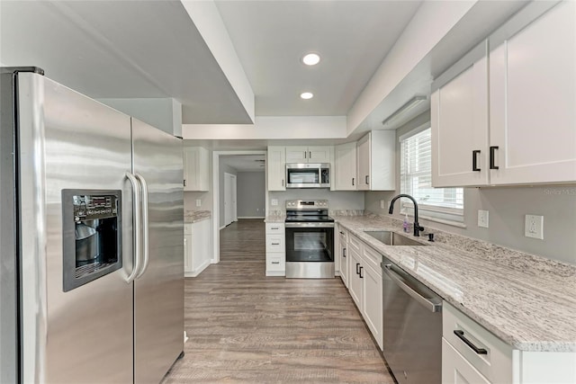 kitchen featuring sink, white cabinetry, light stone counters, light wood-type flooring, and stainless steel appliances