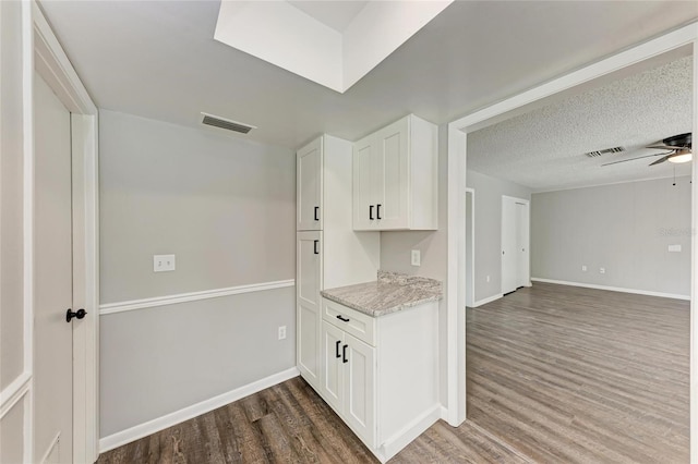 kitchen featuring dark hardwood / wood-style floors, white cabinets, ceiling fan, light stone countertops, and a textured ceiling