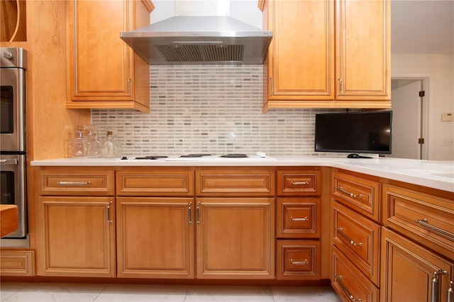 kitchen featuring white stovetop, backsplash, double oven, light stone countertops, and wall chimney exhaust hood