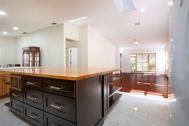 kitchen with stainless steel microwave, wooden counters, a skylight, and a kitchen island