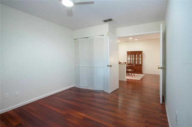 unfurnished bedroom featuring ceiling fan, dark wood-type flooring, a textured ceiling, and a closet