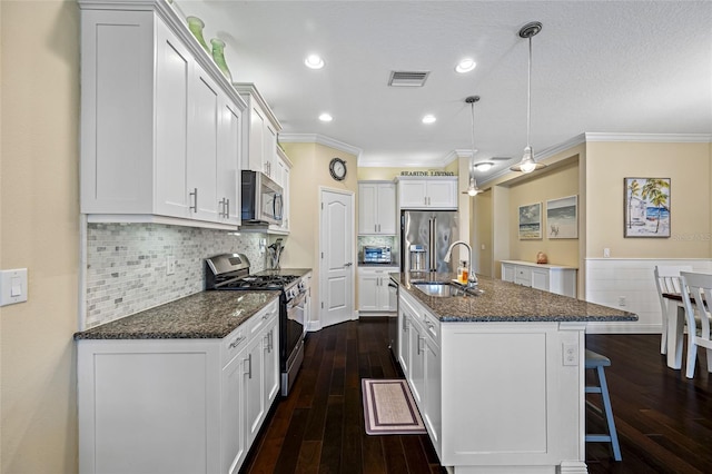 kitchen with sink, decorative light fixtures, appliances with stainless steel finishes, a kitchen island with sink, and white cabinets