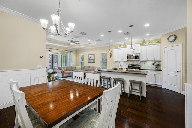 dining room with sink, crown molding, dark wood-type flooring, ceiling fan, and a raised ceiling