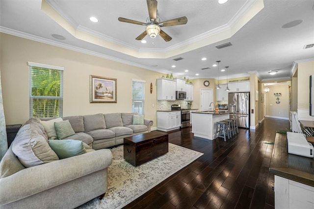 living room with dark hardwood / wood-style floors, sink, ceiling fan, a raised ceiling, and crown molding