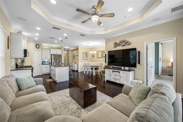 living room featuring a raised ceiling, crown molding, dark hardwood / wood-style floors, and ceiling fan with notable chandelier