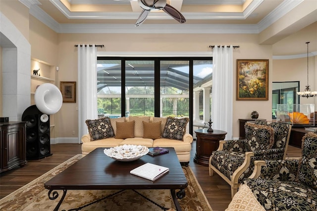 living room featuring dark wood-type flooring, ornamental molding, a raised ceiling, and ceiling fan with notable chandelier