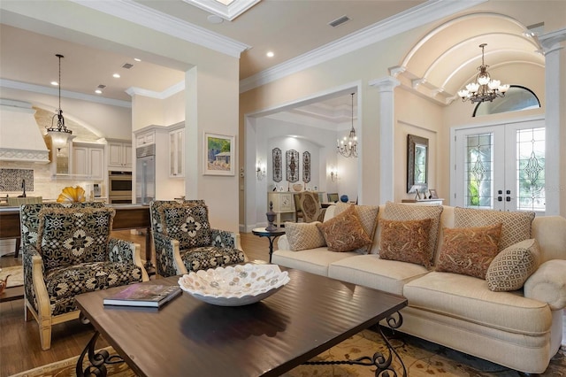 living room with ornate columns, a chandelier, ornamental molding, dark wood-type flooring, and french doors