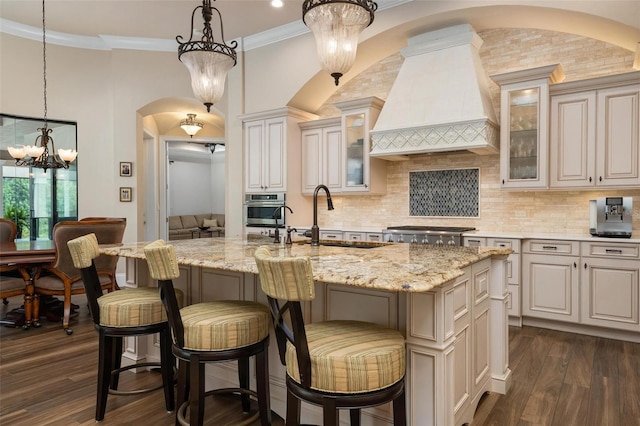 kitchen featuring custom exhaust hood, pendant lighting, a kitchen island with sink, and stainless steel oven