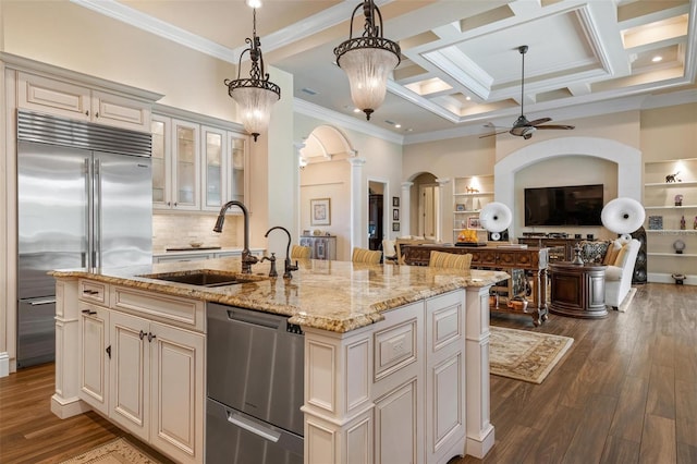 kitchen featuring decorative light fixtures, an island with sink, sink, light stone counters, and stainless steel appliances