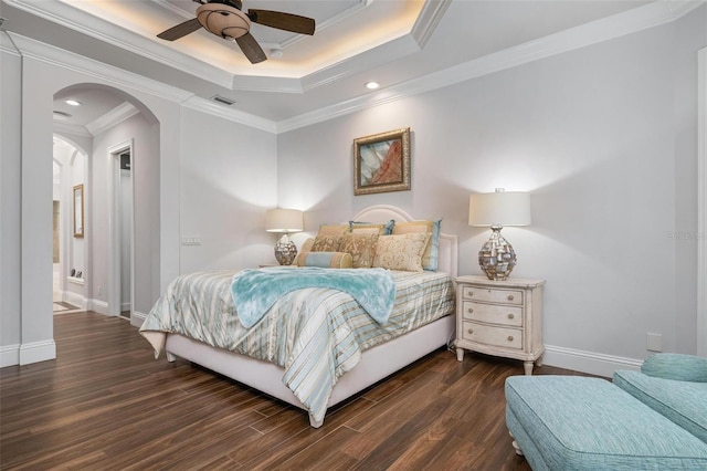 bedroom with ornamental molding, dark wood-type flooring, ceiling fan, and a tray ceiling