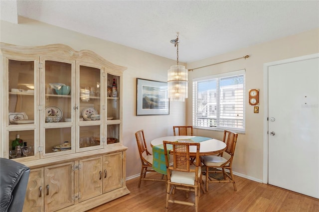 dining area with a notable chandelier, a textured ceiling, and light wood-type flooring