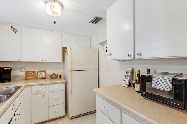 kitchen featuring sink, white cabinets, white fridge, light tile patterned floors, and a textured ceiling