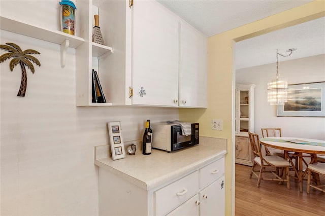 kitchen featuring a textured ceiling, light wood-type flooring, hanging light fixtures, and white cabinets