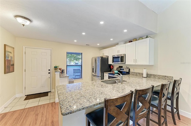 kitchen with appliances with stainless steel finishes, sink, white cabinets, a kitchen breakfast bar, and kitchen peninsula