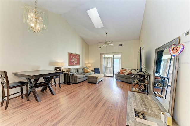 living room featuring high vaulted ceiling, ceiling fan with notable chandelier, a skylight, and light hardwood / wood-style floors